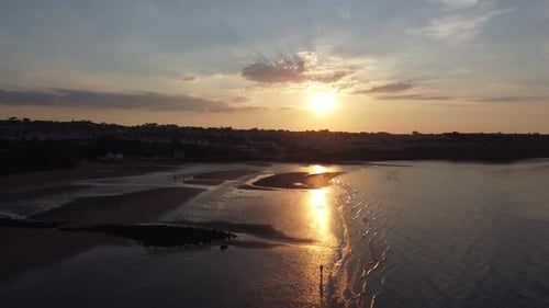 Sunset rays beam fiery golden colours across relaxing beach ocean coastline aerial view pull away sl