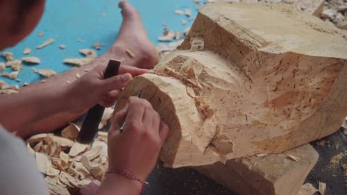 Vue rapprochée des mains d'un artiste balinais qui utilise un ciseau et un maillet pour sculpter le front rugueux