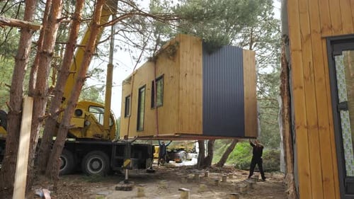 Crane Lifting Modern Prefab Cabin Into Place in Wooded Area