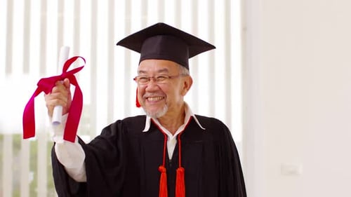 Asian elderly in cap and gown smile and celebration proud success graduate. Cheerful senior man hold