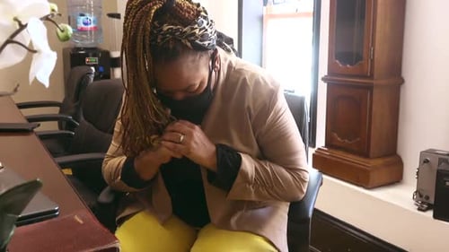 Woman with Braids Clasps Hands in Office Setting