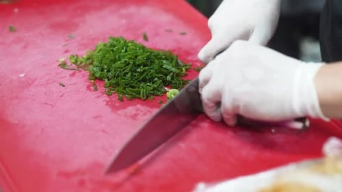 Chef hands cutting green onion on red cutting board, close up. Cutting green onion with a kitchen kn