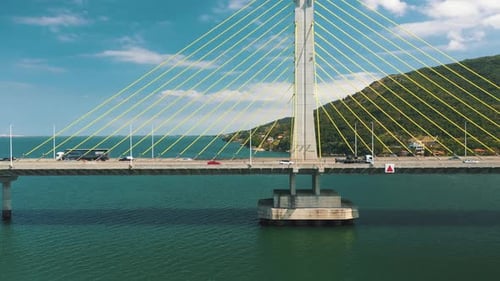 Drone aerial side panning view of concrete cable-stayed bridge traffic above turquoise color ocean