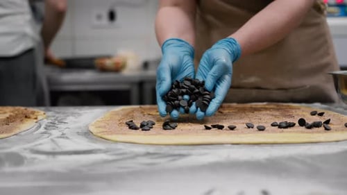 Chef Sprinkles Chocolate Chips onto Dough in Kitchen