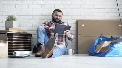 Young man browsing tablet computer at new home after moving in
