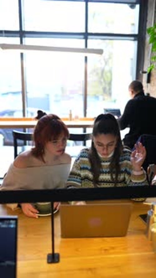 Young Female Friends Working Together with Laptop Computer at Outdoor Cafe