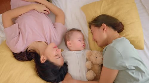 Asian lesbian couple lovingly caring for and raising their baby boy at home.