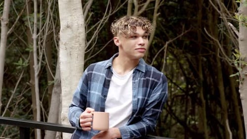 Young man enjoying coffee outdoors in forest, wearing casual plaid shirt