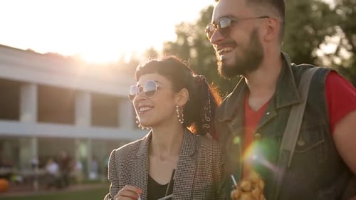 Casal hippie estiloso caminhando comendo sorvete e waffles rindo no parque da cidade, jovem romântico