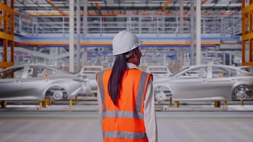 Dos d'une ingénieure asiatique marchant dans une usine automobile