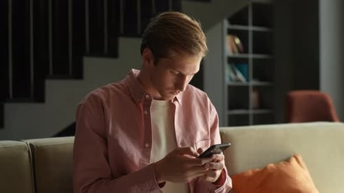 Young Man Using Smartphone Sitting on Sofa Indoors
