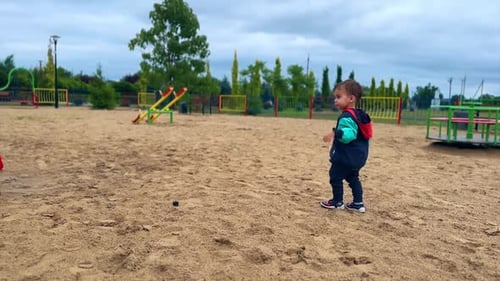 Caucasian child is on the playground on grey dull daytime.
