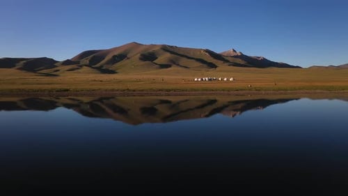 Epic cinematic drone shot of the small yurt village sitting beside the Song-Kol lake in Kyrgyzstan,