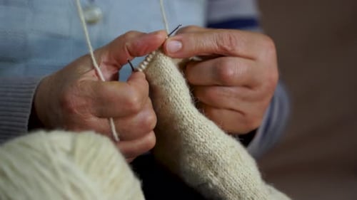 Grandmother hands knitting woolen handiwork hobby craft holding needles by fingers, close up