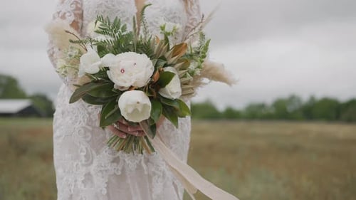 Novia con flores blancas de pie en el campo el día de la boda en cámara lenta