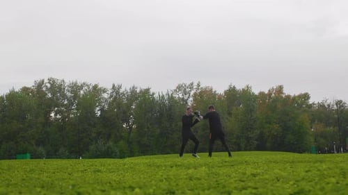 Two Men Sparring Outdoors in a Grassy Park