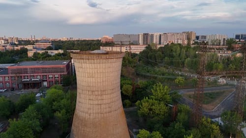 Drohnenaufnahme eines Kühlturms in der Nähe von städtischen Gebäuden und Grünanlagen bei Sonnenuntergang