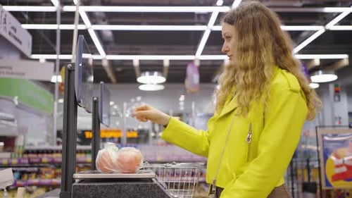 Young Woman in Bright Yellow Jacket Weighs Bag of Produce on Digital Scale at Selfservice Station in