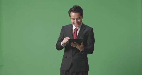 An Asian Business Man Smiling While Using Tablet On Green Screen Background In The Studio