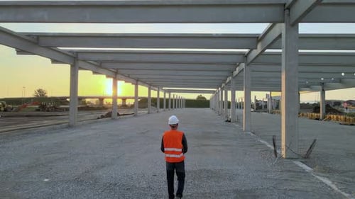 View Behind Civil Engineer Walking Around At Construction Site For Inspection. drone shot
