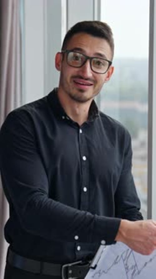 Businessman in black shirt, trousers and glasses holding a paper with chart.