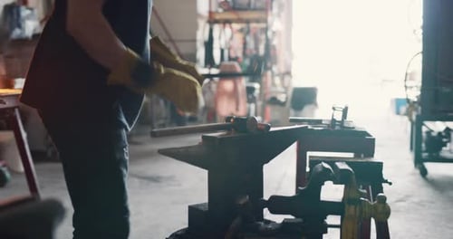 Professional blacksmith hammering hot metal iron in workshop with soft day lighting