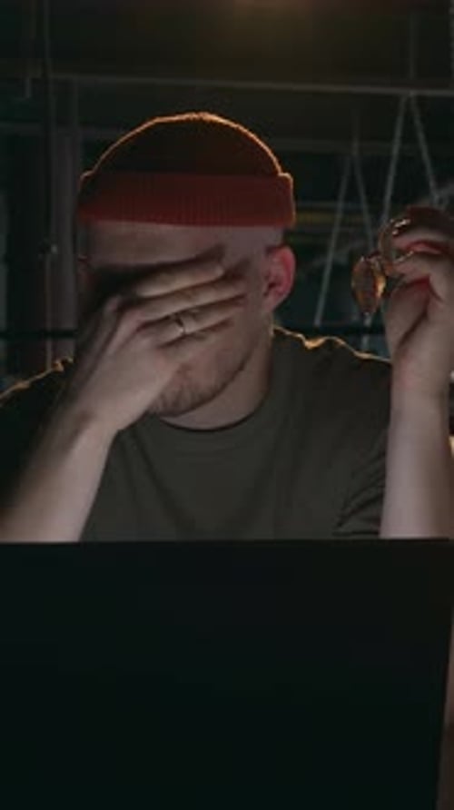 Tired Man Removing Glasses and Rubbing Eyes While Working on Laptop