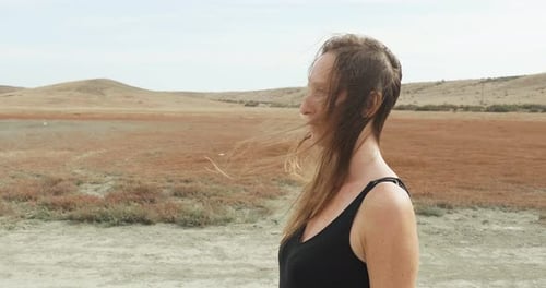 A Woman in a Black Dress Walks Along a Dirt Road Against a Desert Background Side View A Symbolic
