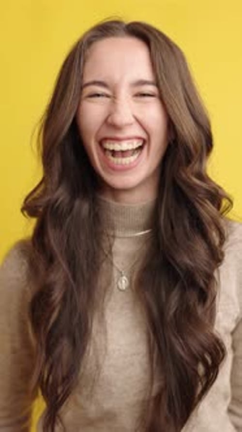 Young Woman Bursting Into Joyful Laughter on Yellow Background