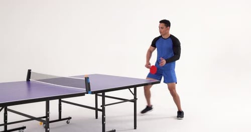 Playing table tennis, man hitting ball with paddle in studio setting