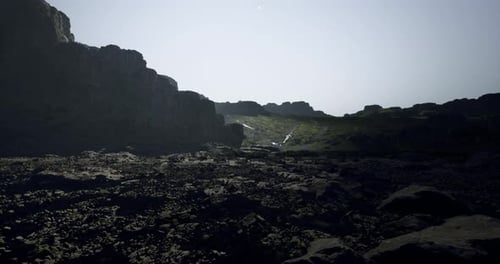 Dramatic Rocky Landscape with Distant Waterfall Under Bright Sunlight