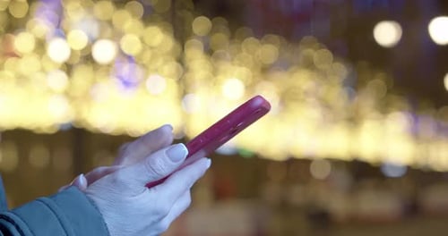 Closeup Video of Female Hands with a Smartphone with a Night Christmas Lights on Background