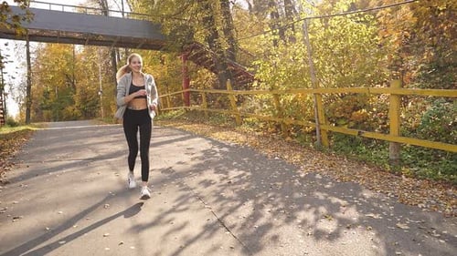 a Young Woman with Blonde Hair in Sportswear is Doing Sports Running in an Autumn Park in the Fresh
