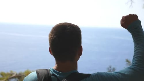 Cheerful Hiker with Backpack Rejoicing Success on Edge of Mountain Victoriously Raising Hand Male