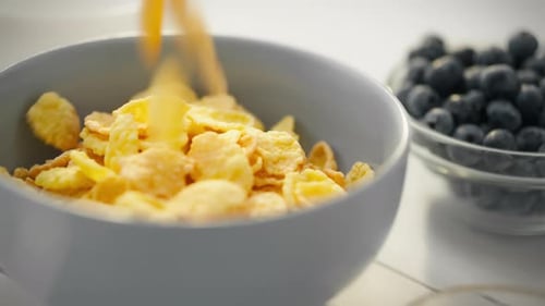Pouring Cornflakes into a Bowl with Blueberries