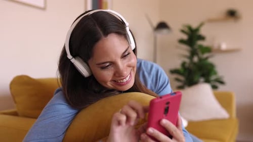 Glückliche junge Frau benutzt Handy, während sie sich zu Hause auf dem Sofa entspannt