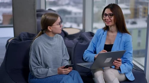 Long haired brunette wearing blue jacket explains her point to a colleague showing laptop files.