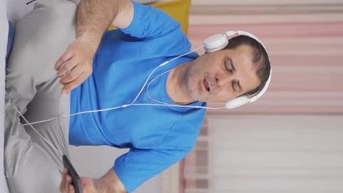 Vertical video of Man listening to music with headphones is unhappy and sad.