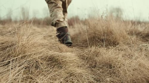 Military Woman Moving Across Desolate Field with Dry Yellow Grass