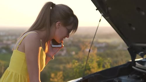 Young Female Driver Talking on Mobile Phone Standing Near Her Car with Open Hood Having Engine