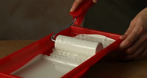 Applying White Paint to Roller on Red Tray