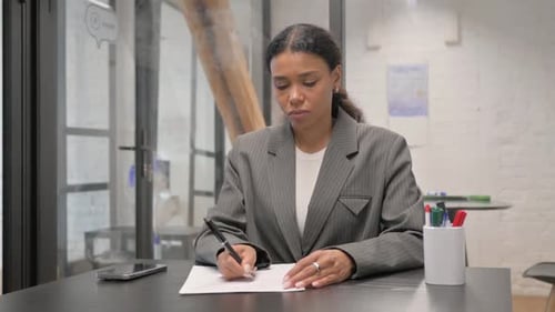 African American Businesswoman Writing while Sitting at Office