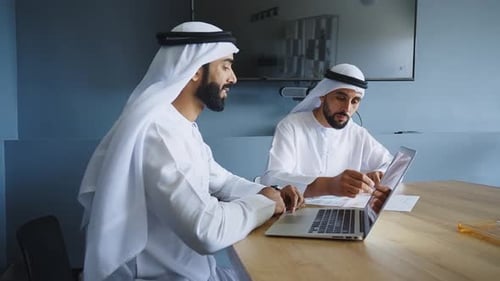 two businessmen working together in a modern office in the united arab emirates.