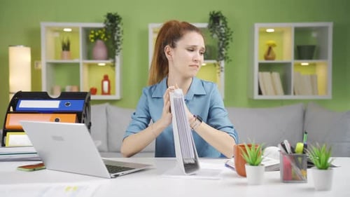 Frustrated Woman Looks Through Binder at Desk