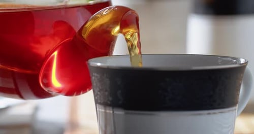 Black Hot Tea is Poured From a Glass Teapot Into a Cup Slow Motion