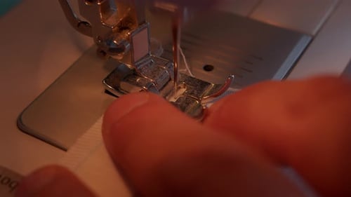Close up of slow moving needle of sewing machine and fingers of operator pulling fabric through.