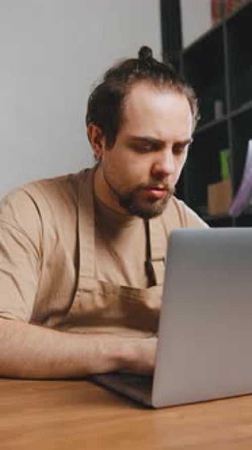 Barista Works on Laptop to Manage Coffee Orders in Artisan Cafe During Busy Afternoon Hours While