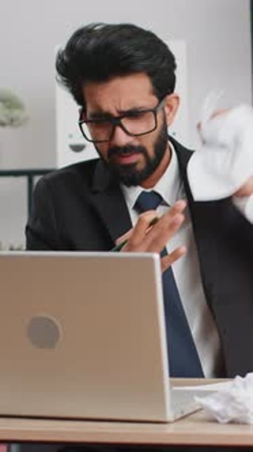 Wütender Mann, der im Heimbüro arbeitet und zerknittertes Papier wirft und bei der Arbeit einen Nervenzusammenbruch erleidet