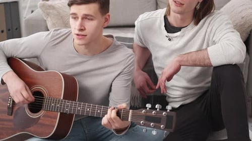 Two Young Adults Play Guitar and Sing Together