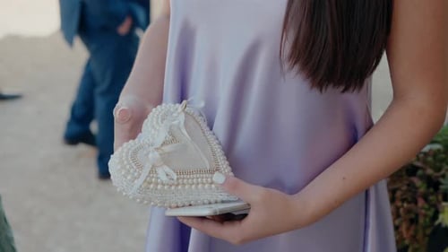 delicate hand holds a heart-shaped, pearl-embellished ring pillow, symbolizing love and commitment